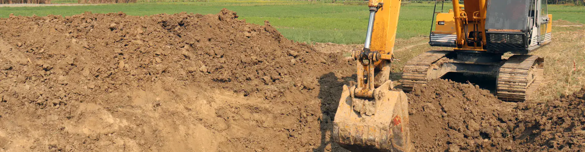 Excavator bucket cutting into a stockpile of soil on a cleared paddock