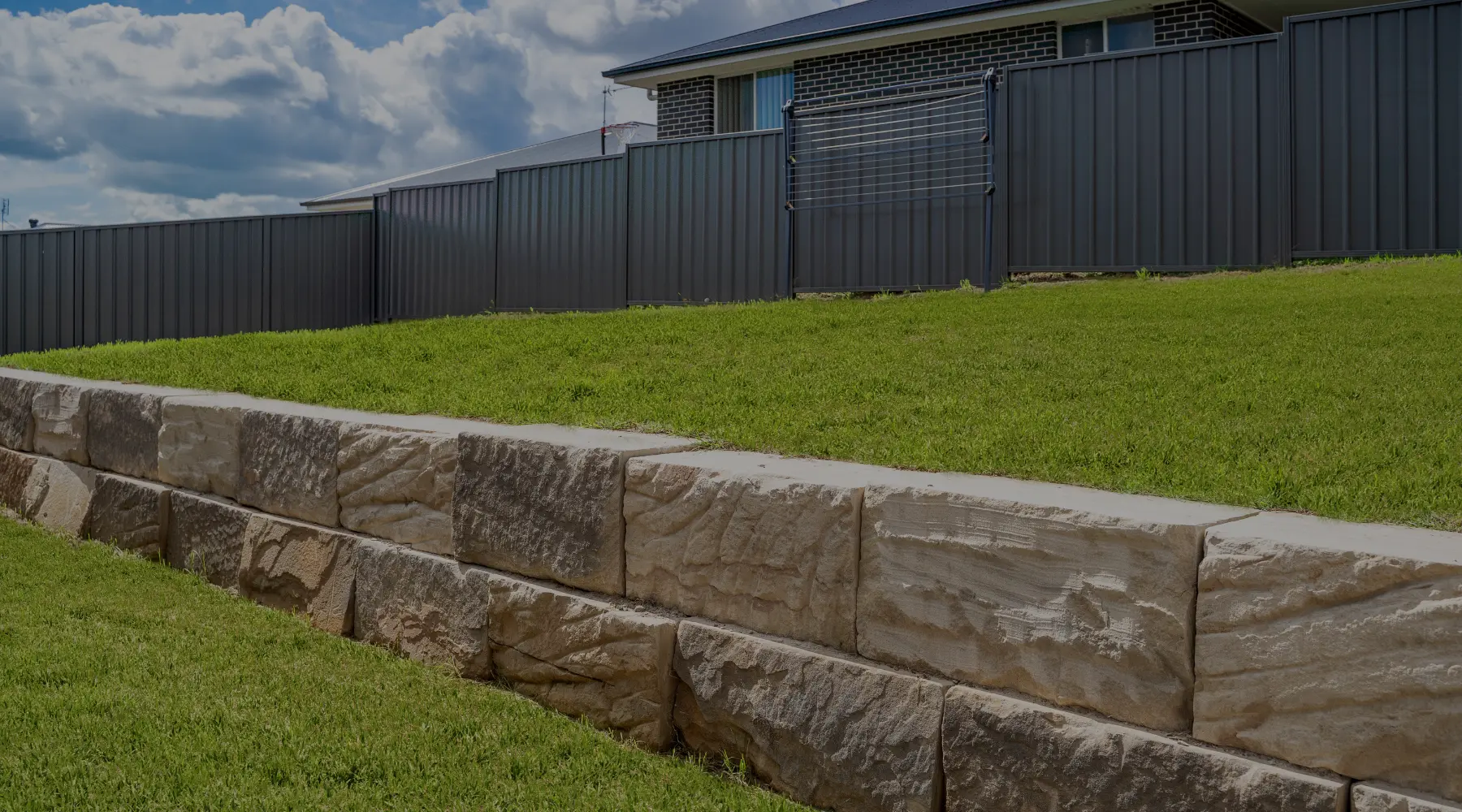 Sandstone block retaining wall along a new lawn, with a dark steel fence behind