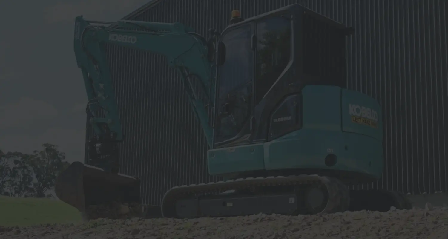 Excavator on a levelled gravel pad in front of a steel shed